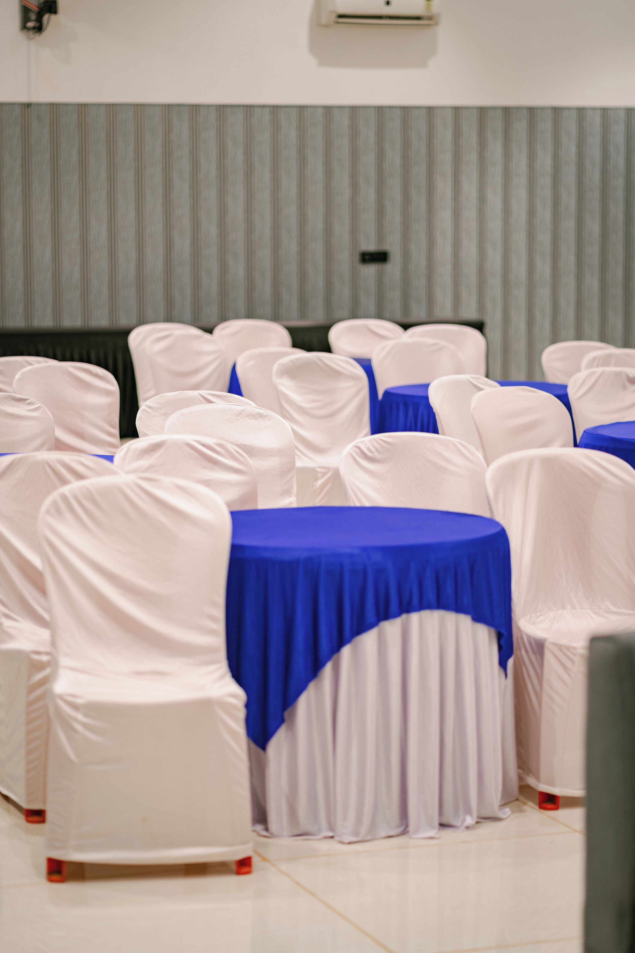 Rows of tables with blue tablecloths and white chairs with white covers.