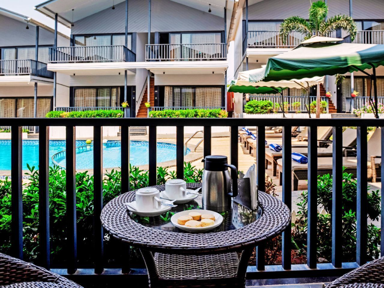 A balcony with a table set for breakfast, overlooking a pool and a building with multiple balconies.