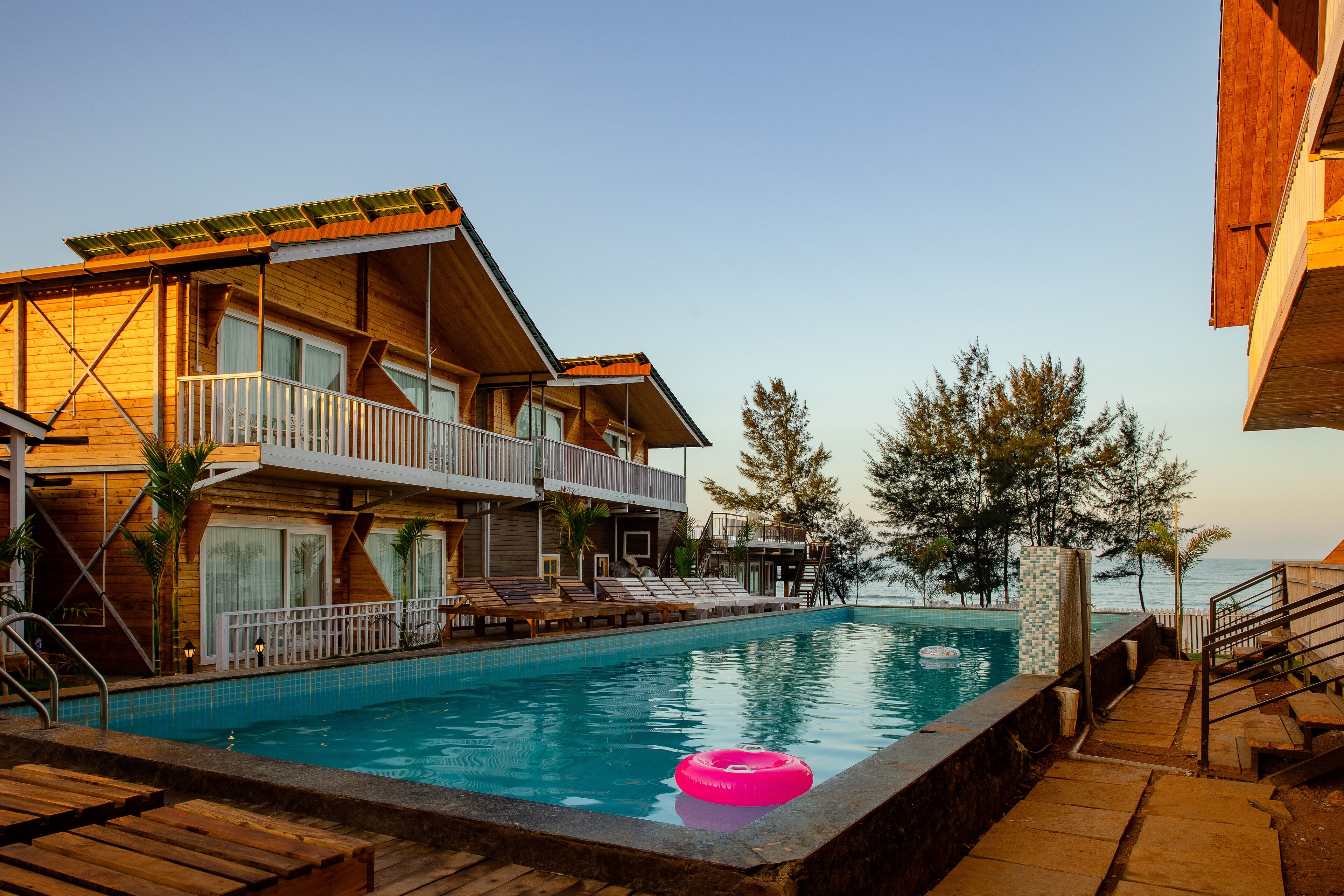 A wooden building with a pool, a pink float, and a view of the sea.