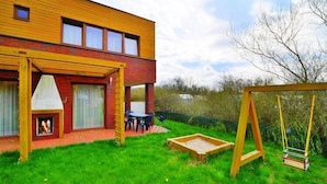 A modern house with a wooden exterior, a patio with a table and chairs, and a swing set. - Holiday home with a private garden (Sarbinowo)