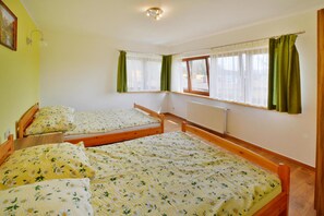 Una habitación con dos camas de madera, un radiador, una ventana con cortinas y una lámpara fijada a la pared.