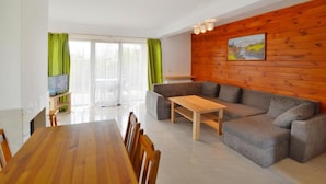 Un salon moderne avec un mur en bois, un canapé gris, une table basse en bois et un coin repas comprenant une table et des chaises en bois.
