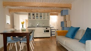 A modern kitchen with wooden beams, a dining area with a table and chairs, and a sofa with blue cushions. - historic cottage in scenic Dutch landscape at IJsselmeer (Andijk)