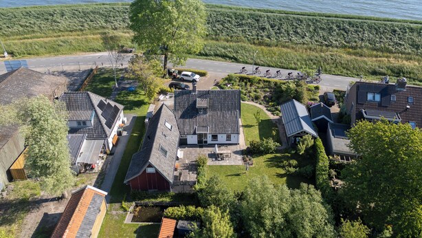 An aerial view of a residential area with houses, a road, and a body of water in the background. - historic cottage in scenic Dutch landscape at IJsselmeer (Andijk)