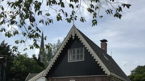 A traditional house with a steeply pitched roof, a brick exterior, and a small front porch. - historic cottage in scenic Dutch landscape at IJsselmeer (Andijk)