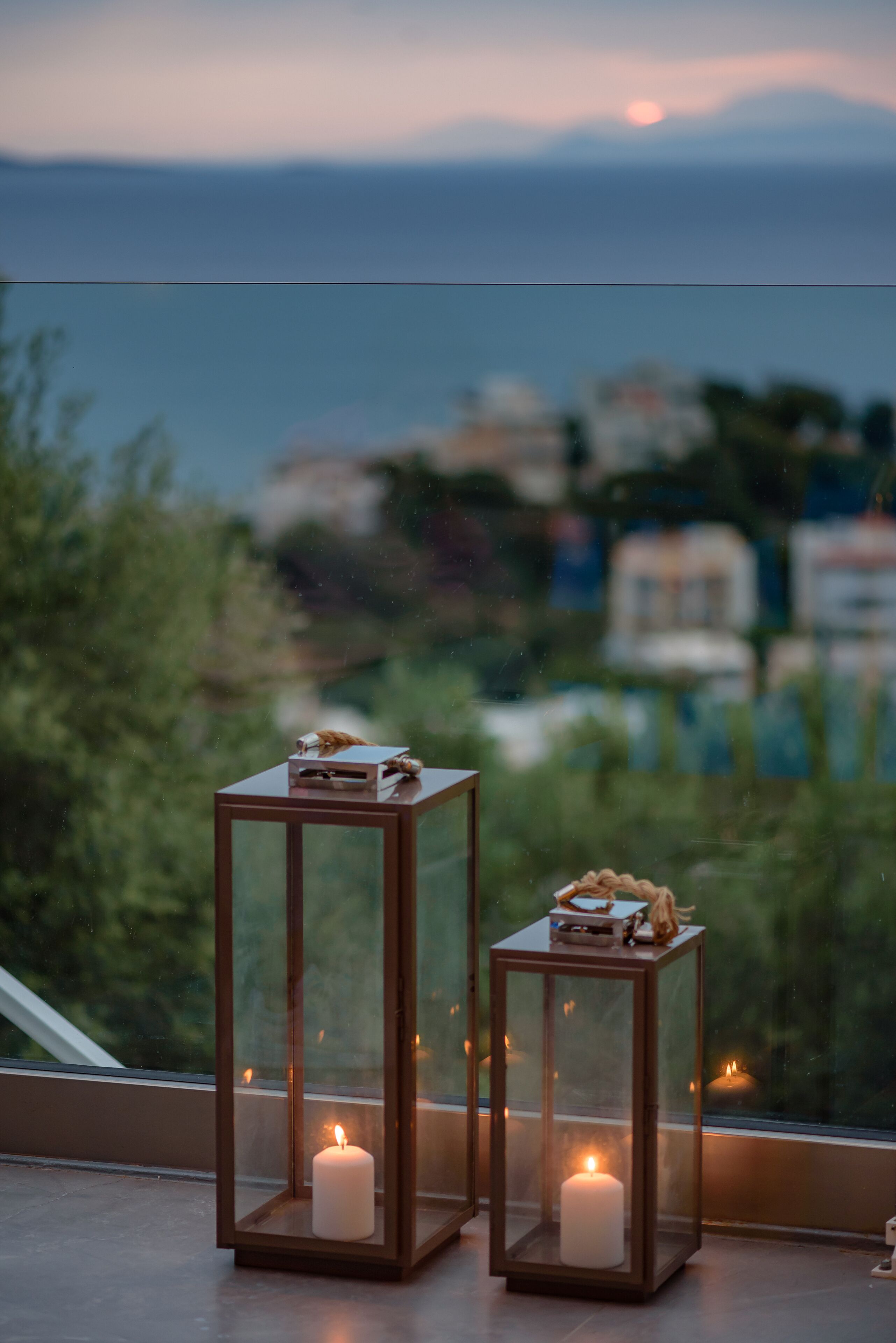 Dos faroles cuadrados con velas en un balcón con vistas al mar.