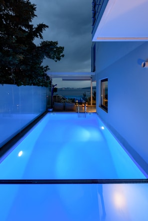 A modern outdoor pool area with a view of the sea at dusk.