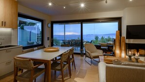 A modern kitchen with a dining area, large windows with a view, and a cozy seating area with a fireplace. - Greek Zen villa - stunning sea view -top of the hill in Athens Riviera (PWV6+C39 Saronida, Greece)