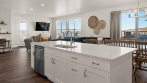 A modern kitchen with a large island, white cabinetry, and a dining area with wooden chairs. - TNT Sun Adventures: Hot Tub, Arcade, Air Hockey (Washington)