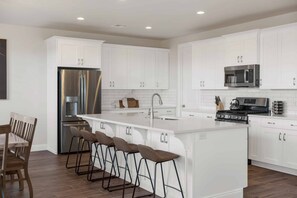 Una cocina moderna con armarios blancos, electrodomésticos de acero inoxidable y una isla central con taburetes de bar.