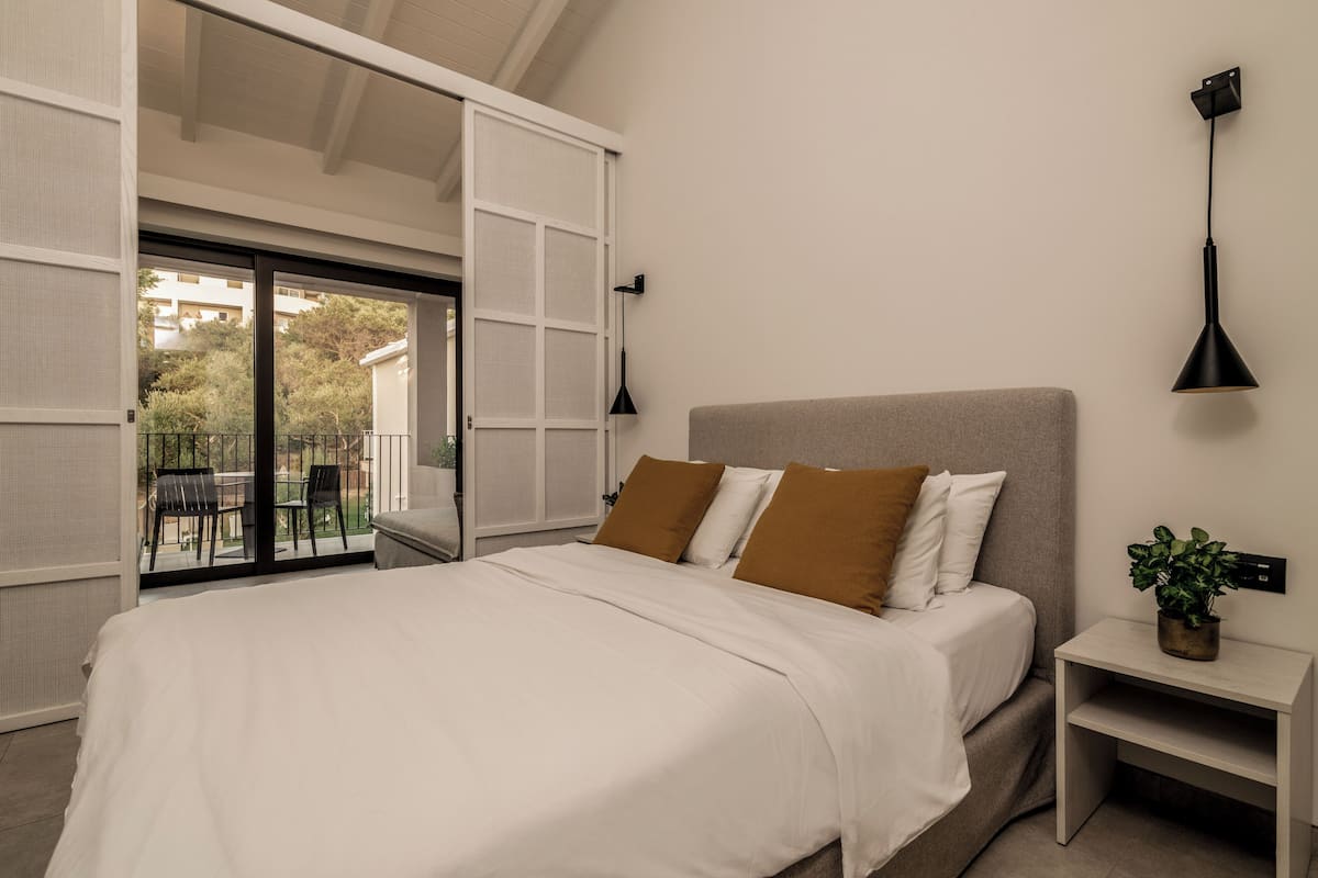 A bedroom with a bed, a nightstand, a wall-mounted lamp, and a sliding door to a balcony.
