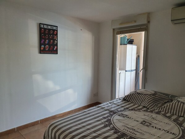 A bedroom with a striped bedspread, a poster of The Rolling Stones on the wall, and a door leading to a bathroom. - Joli 2 Pièces à L'entrée des Calanques, à Deux Minutes de la Plage (Marseille)