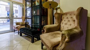 A room with a large, plush armchair, a matching ottoman, and a tall, dark-colored cabinet with glass doors. - Hotel Riviera (Paris)