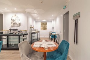 Un comedor con una mesa redonda dispuesta para cuatro, una jaula de pájaros en la pared y una colección de cuadros enmarcados.