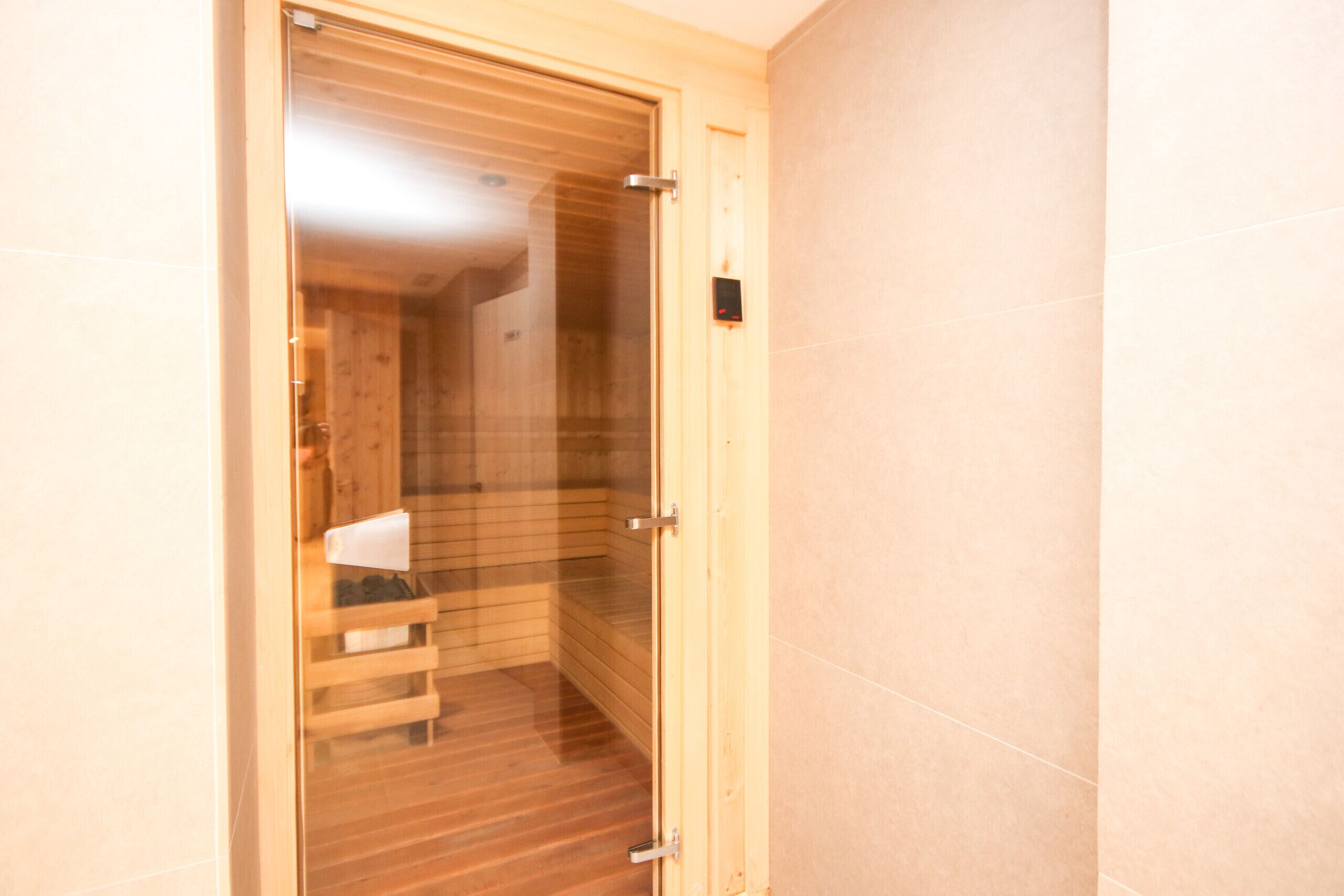 A wooden sauna room with a glass door, a bench, and a control panel on the wall.