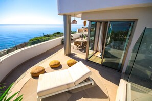 A balcony with a white lounge chair, two round cushions, a glass door leading to a dining area, and a view of the ocean. - Penthouse, Amazing Sea Views, Plunge Pool and BBQ (Mijas Costa)