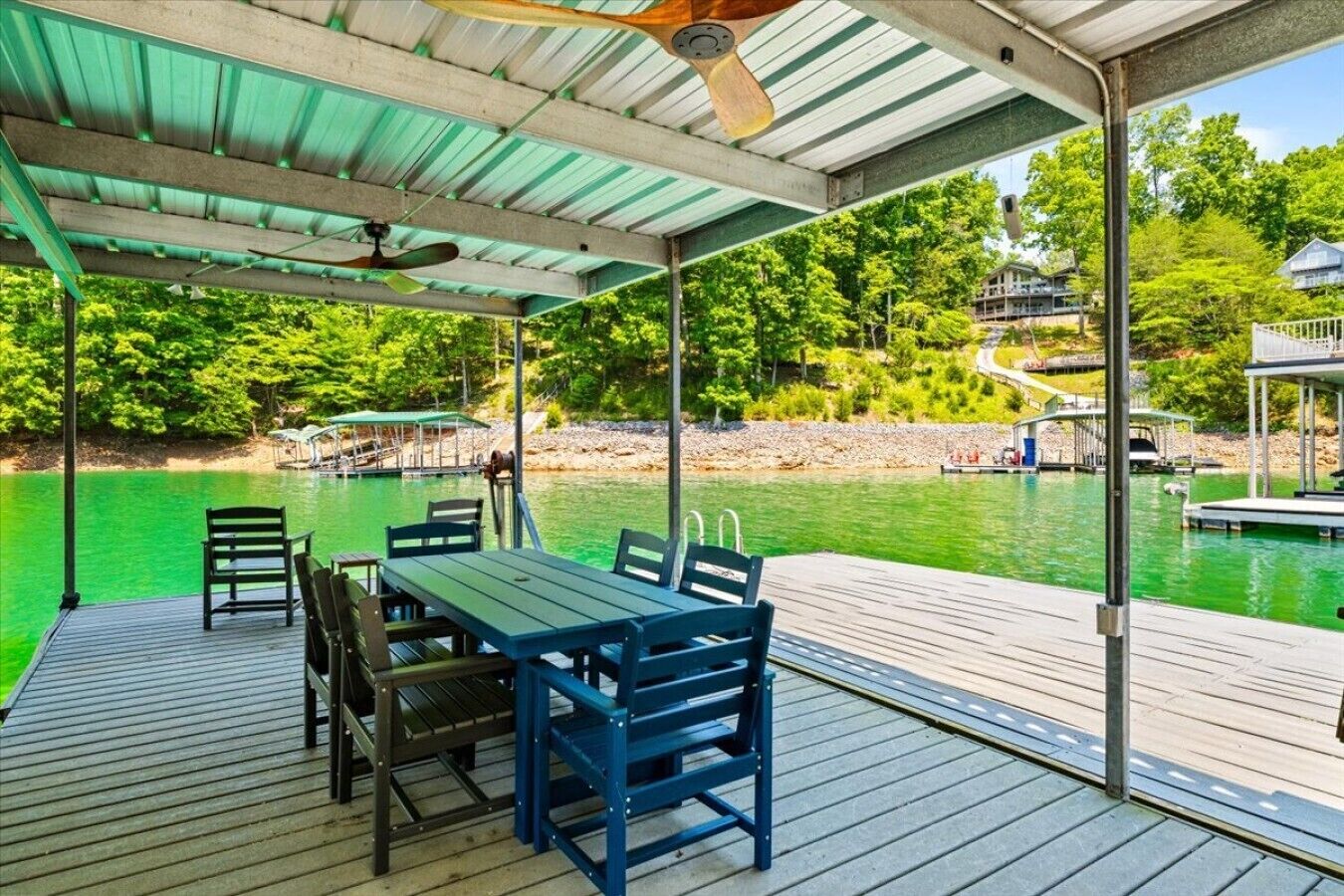 Une terrasse couverte, dotée d’une table et de chaises, qui offre une vue sur une étendue d’eau où se trouvent des quais et des bateaux.
