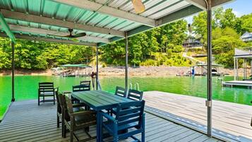 Une terrasse couverte, dotée d’une table et de chaises, qui offre une vue sur une étendue d’eau où se trouvent des quais et des bateaux.