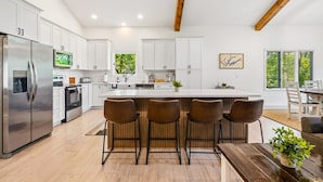 Una cocina moderna con armarios blancos, un refrigerador de acero inoxidable, una isla central con taburetes altos y vigas de madera en el techo.