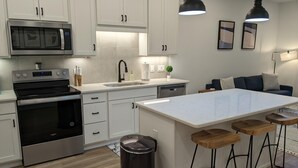 A modern kitchen with white cabinets, stainless steel appliances, a central island with stools, and pendant lighting. - Luxury 1 Bedroom Downtown Traverse City (Traverse City)