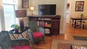A living room with wicker furniture, a flat-screen TV, and a bookshelf. - Barkley-Hayward Cottage (Little Rock)