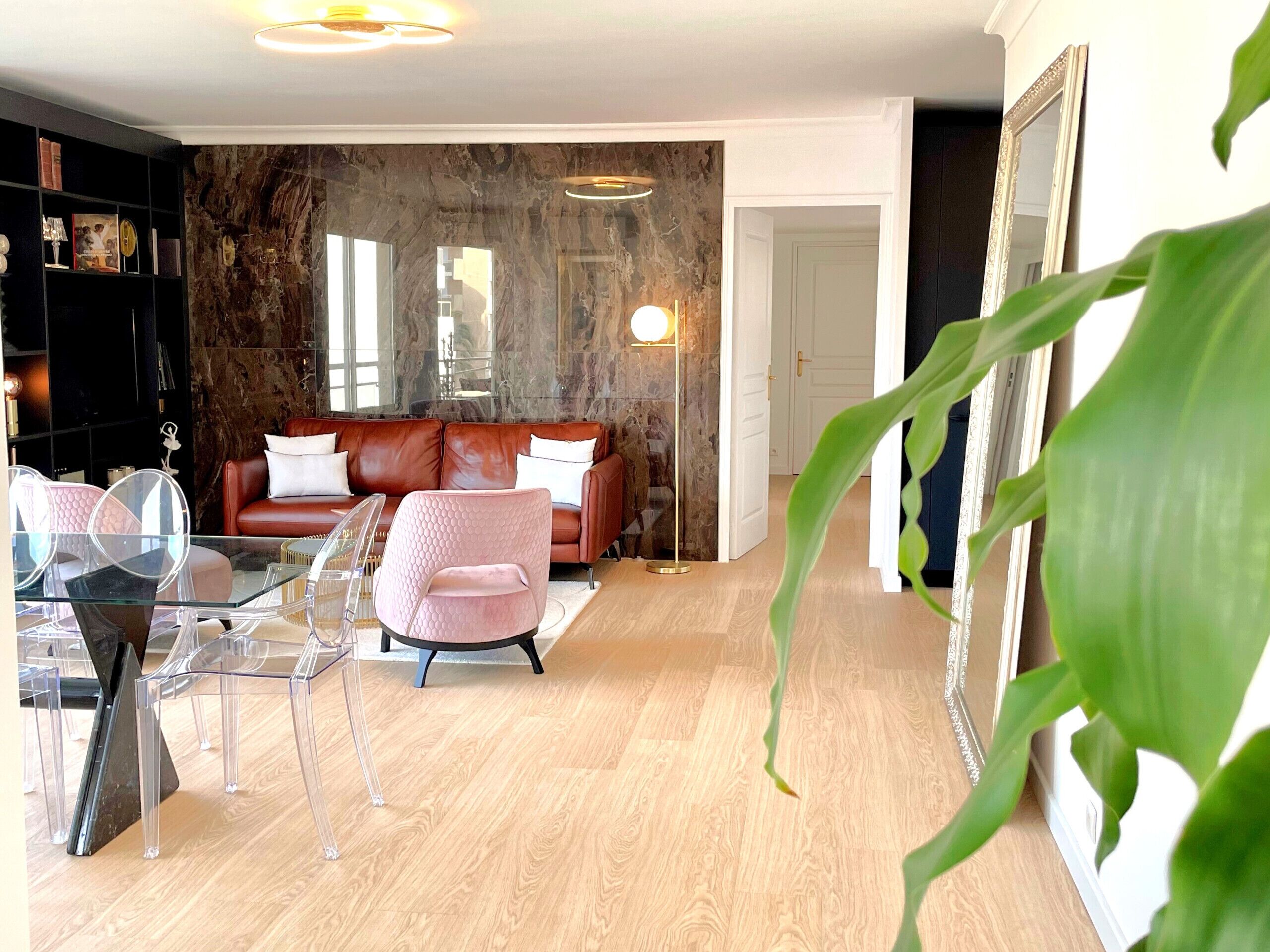 Una sala de estar moderna con un sofá de cuero, muebles de vidrio transparente y una pared de mármol.