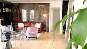 A modern living room with a leather sofa, clear glass furniture, and a marble wall. - Luxury 3 bedroom apartment (Cannes)