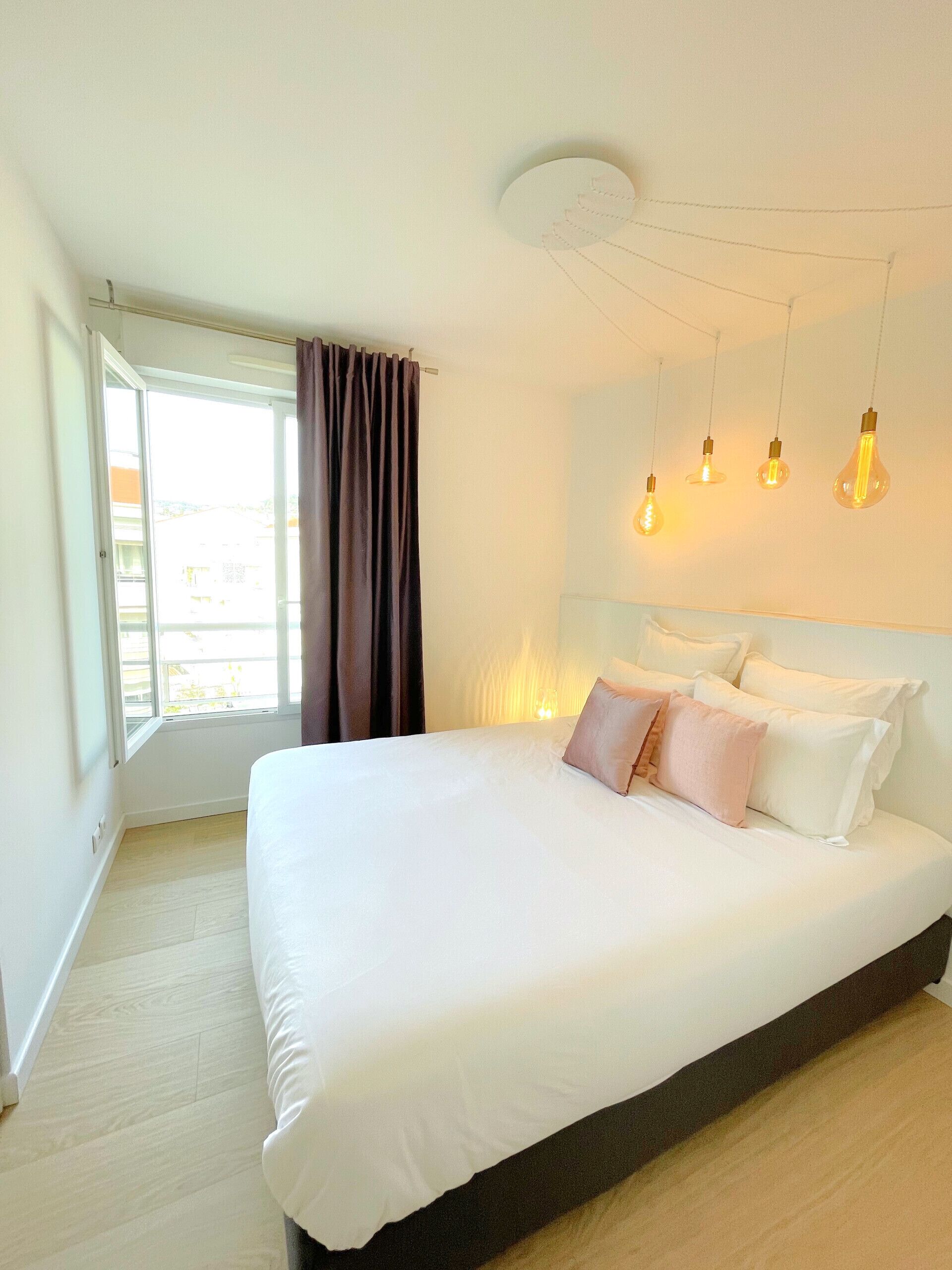 Un dormitorio con una cama grande, una ventana con cortinas y cuatro bombillas colgantes.