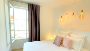 A bedroom with a large bed, a window with curtains, and four hanging light bulbs. - Luxury 3 bedroom apartment (Cannes)