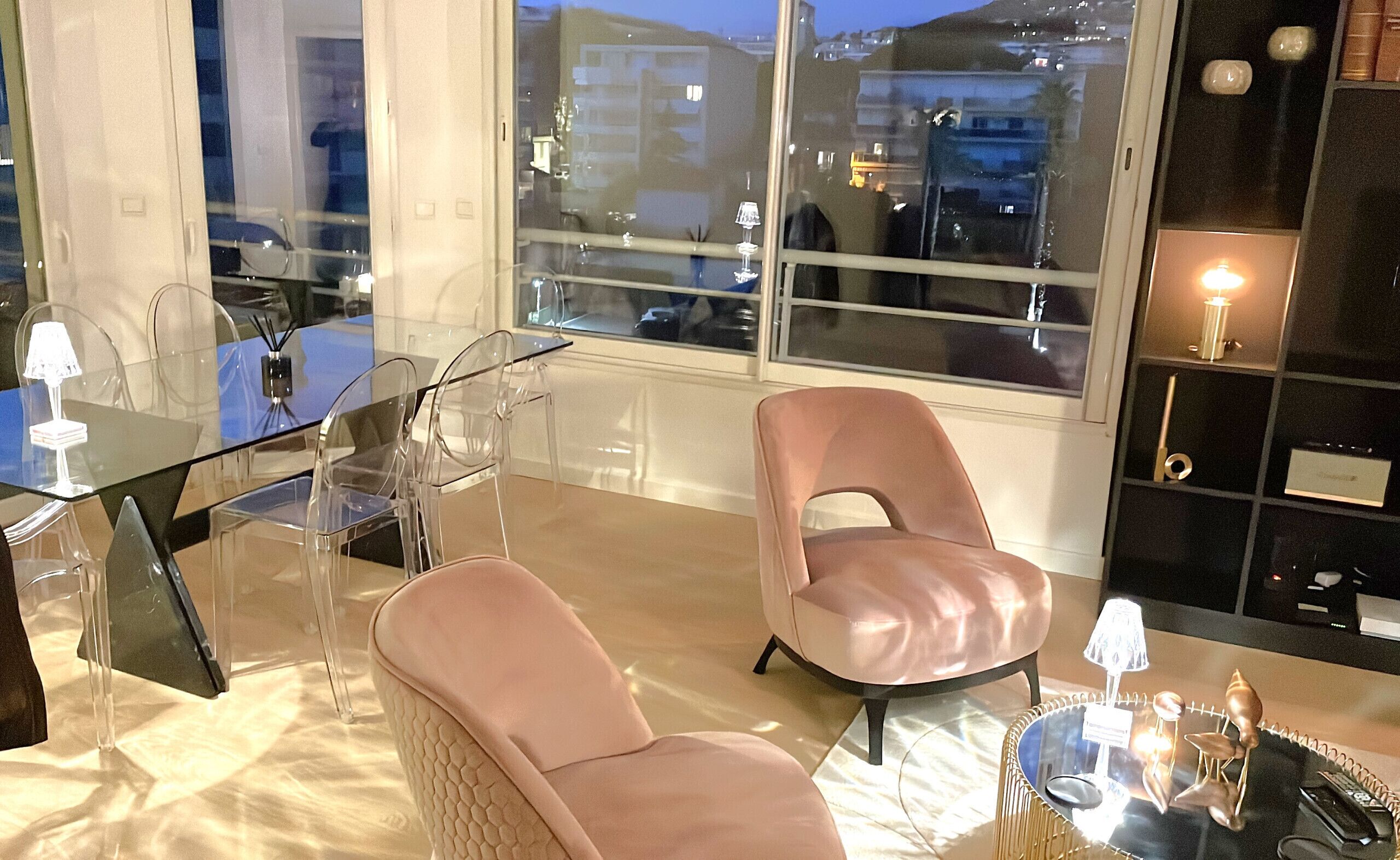 A modern living room with a glass table, two leather chairs, a glass coffee table, and a bookshelf.