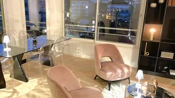 A modern living room with a glass table, two leather chairs, a glass coffee table, and a bookshelf.