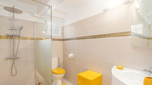 Un bany amb dutxa de vidre, vàter, rentapèns i un armari groc.