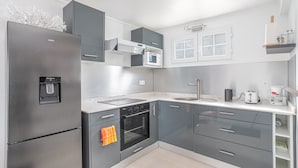 Una cuina moderna amb armaris grisos, un refrigerador d'acer inoxidable, un forn integrat, un microones i una cafetera.