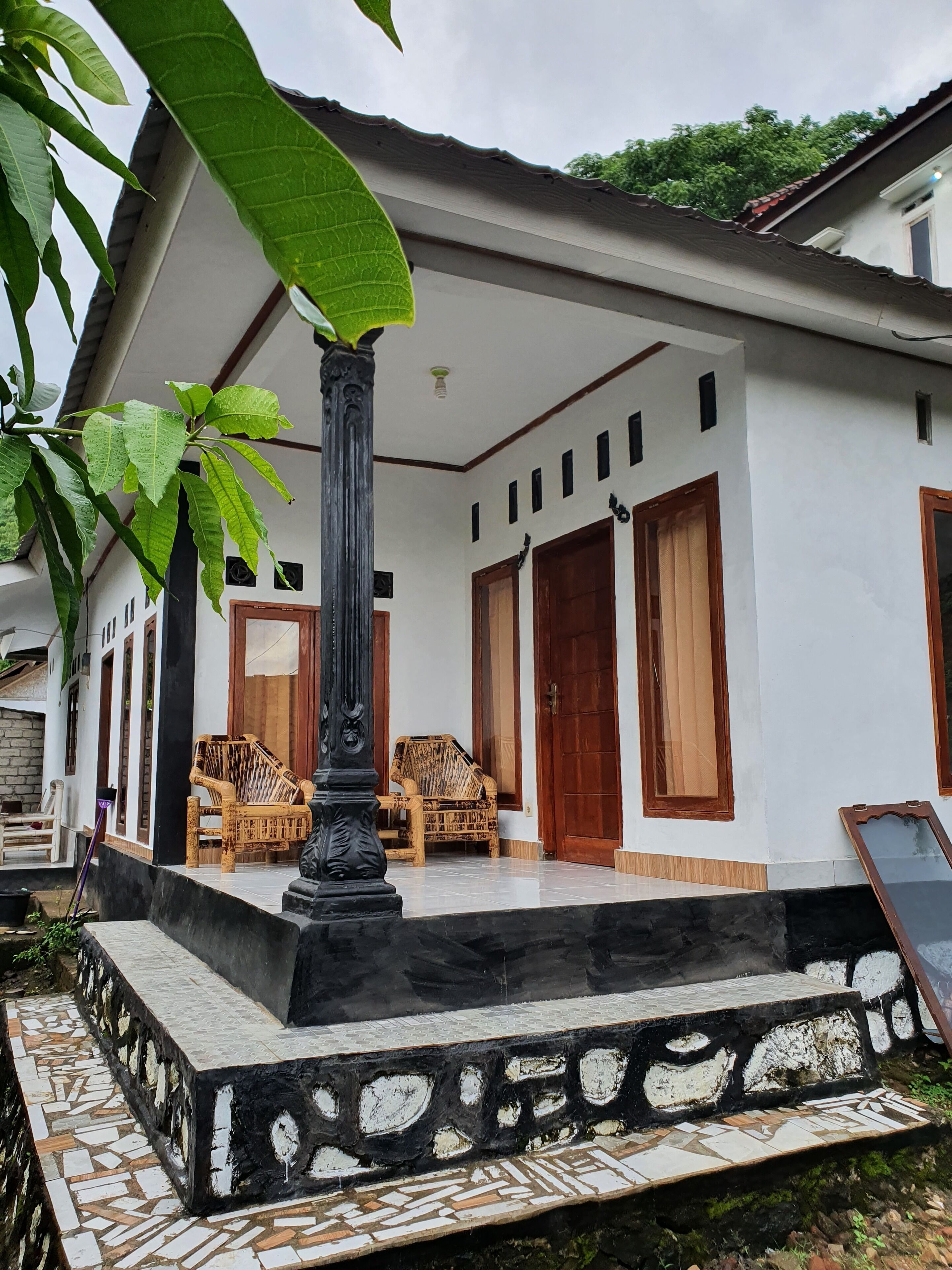 Una casa con veranda, due poltrone in vimini e una pianta grande.
