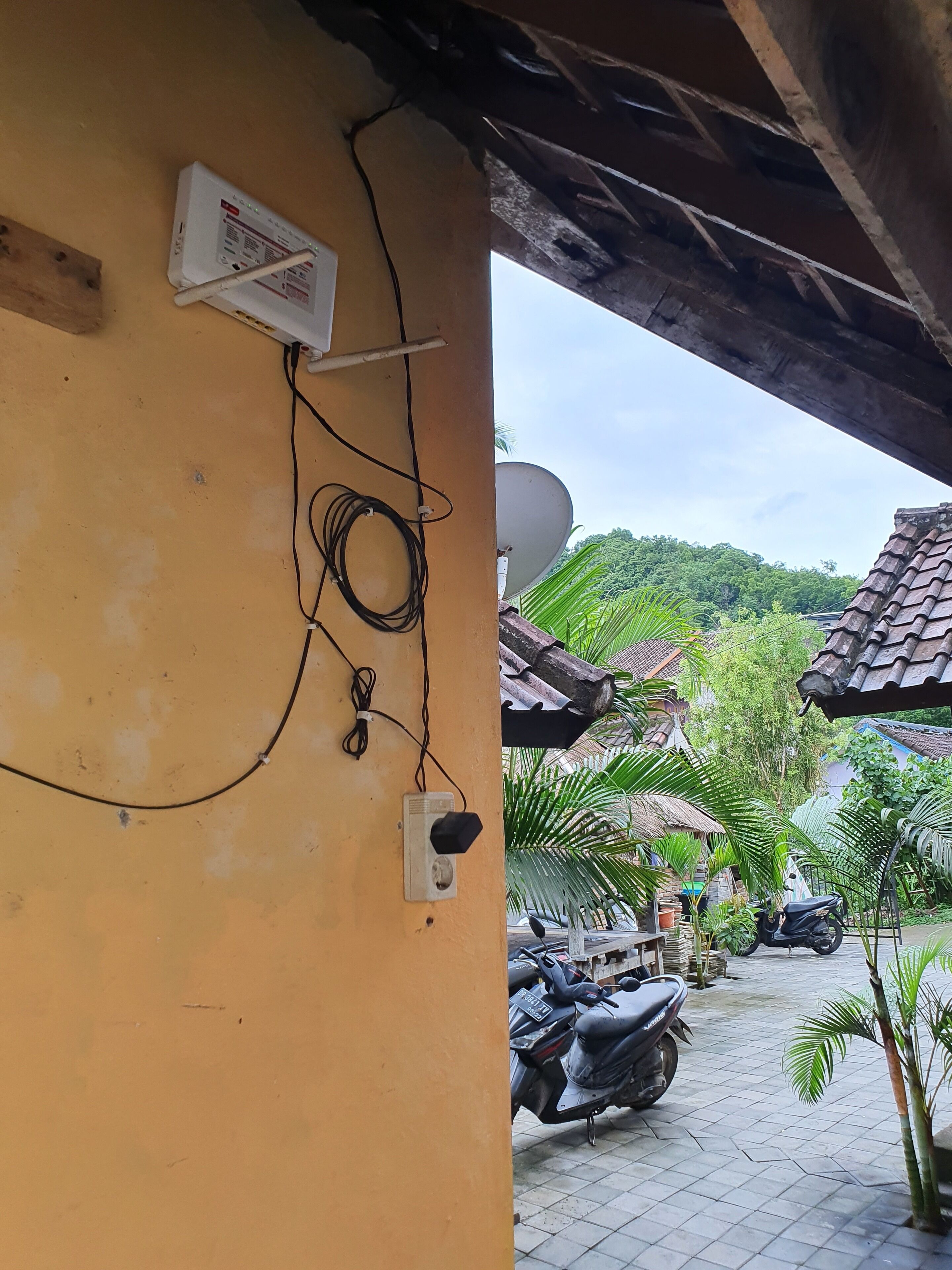 A yellow wall with a satellite dish, a power outlet, and a coiled cable.
