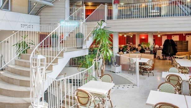 A spacious indoor area with a central staircase, multiple seating areas, and a dining section. - Hotel Saint Sauveur (Lourdes)