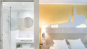 A hotel room with a glass shower, a white sink, a mirror, a bed with white bedding, and a wall with a cityscape silhouette. - Hotel Saint Sauveur (Lourdes)