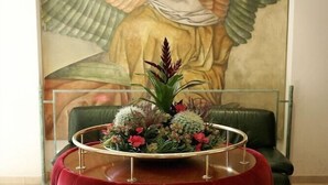 A room with a tufted red sofa, a glass table with a floral centerpiece, and a large painting of an angel in the background. - Hotel Saint Sauveur (Lourdes)