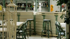 A bar area with green chairs and tables, shelves with bottles, and a decorative lamp. - Hotel Saint Sauveur (Lourdes)