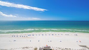 A beach with a wooden walkway leading to the water, a row of beach umbrellas, and a clear blue sky.