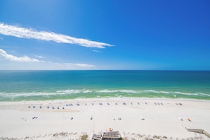 A beach with a wooden walkway leading to the water, a row of beach umbrellas, and a clear blue sky.