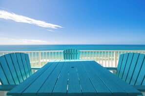 A balcony with a view of the ocean, a table, and two chairs.