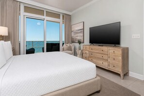 Quarto de hotel com cama grande, televisão de tela plana, cômoda de madeira e varanda com vista para o mar.
