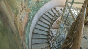 A spiral staircase with a glass railing, surrounded by a mural with classical figures. - Villa Saint Henri (Cannes)