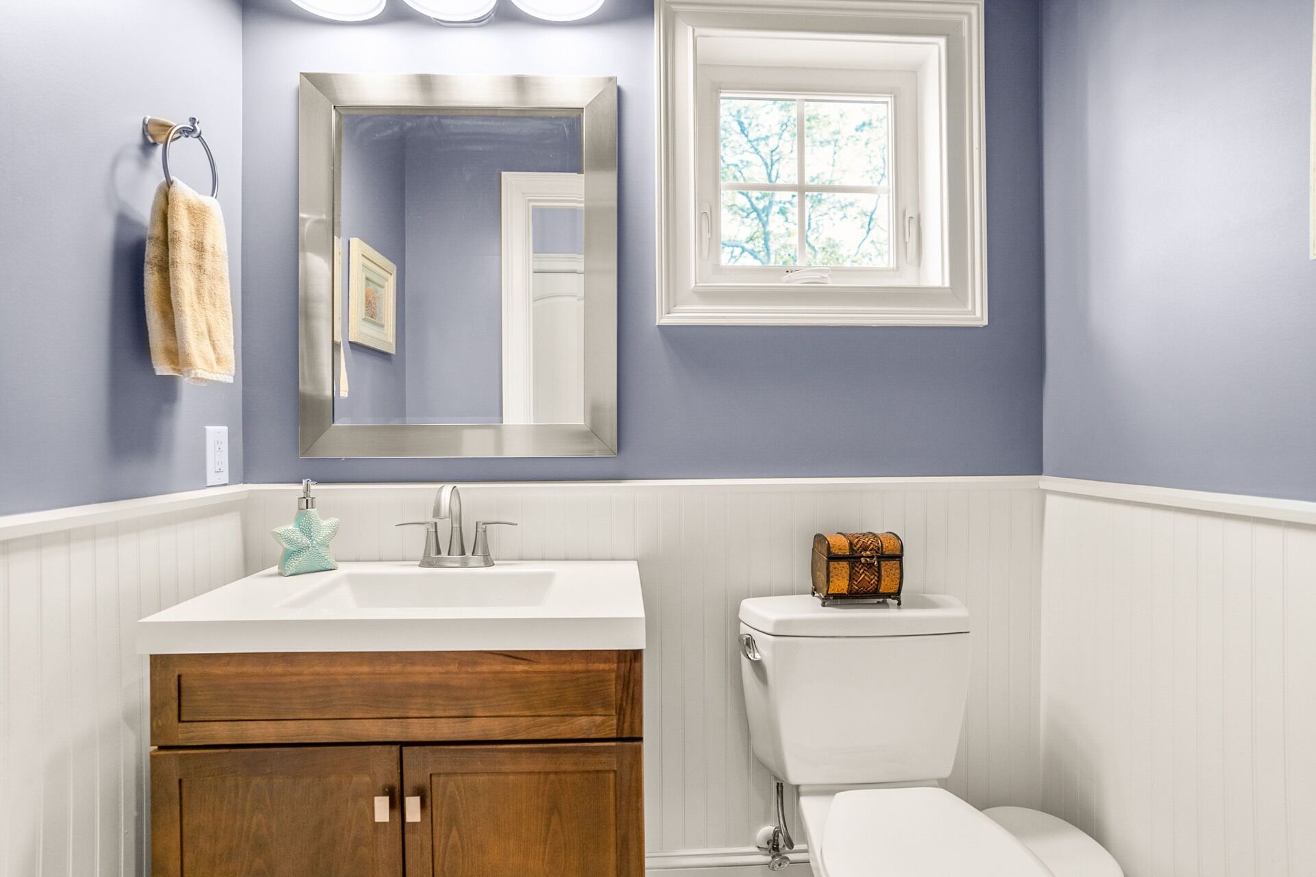 A bathroom with a vanity, a toilet, a mirror, and a window.
