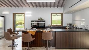 Eine moderne Küche mit Kochinsel, Barhocker, integriertem Backofen und großen Fenstern mit Blick ins Freie.