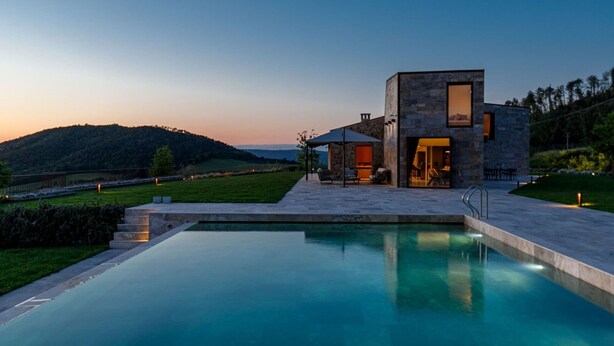 Ein modernes Haus mit Swimmingpool, Naturstein-Fassade und Blick auf die Hügel.