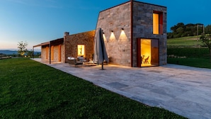 Ein modernes Haus mit Steinaußenwand, Sitzgelegenheit im Freien und Blick auf die Landschaft.