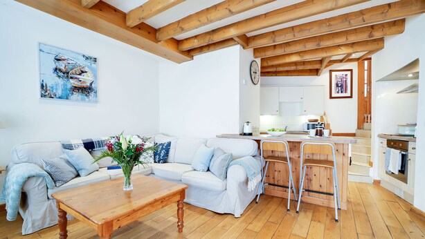 Un salon chaleureux avec une table en bois, un canapé blanc et une cuisine en arrière-plan.