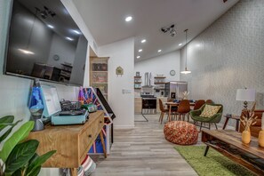 Een moderne woonkamer met een flatscreen televisie, houten meubels, een groene bank en een keuken op de achtergrond.